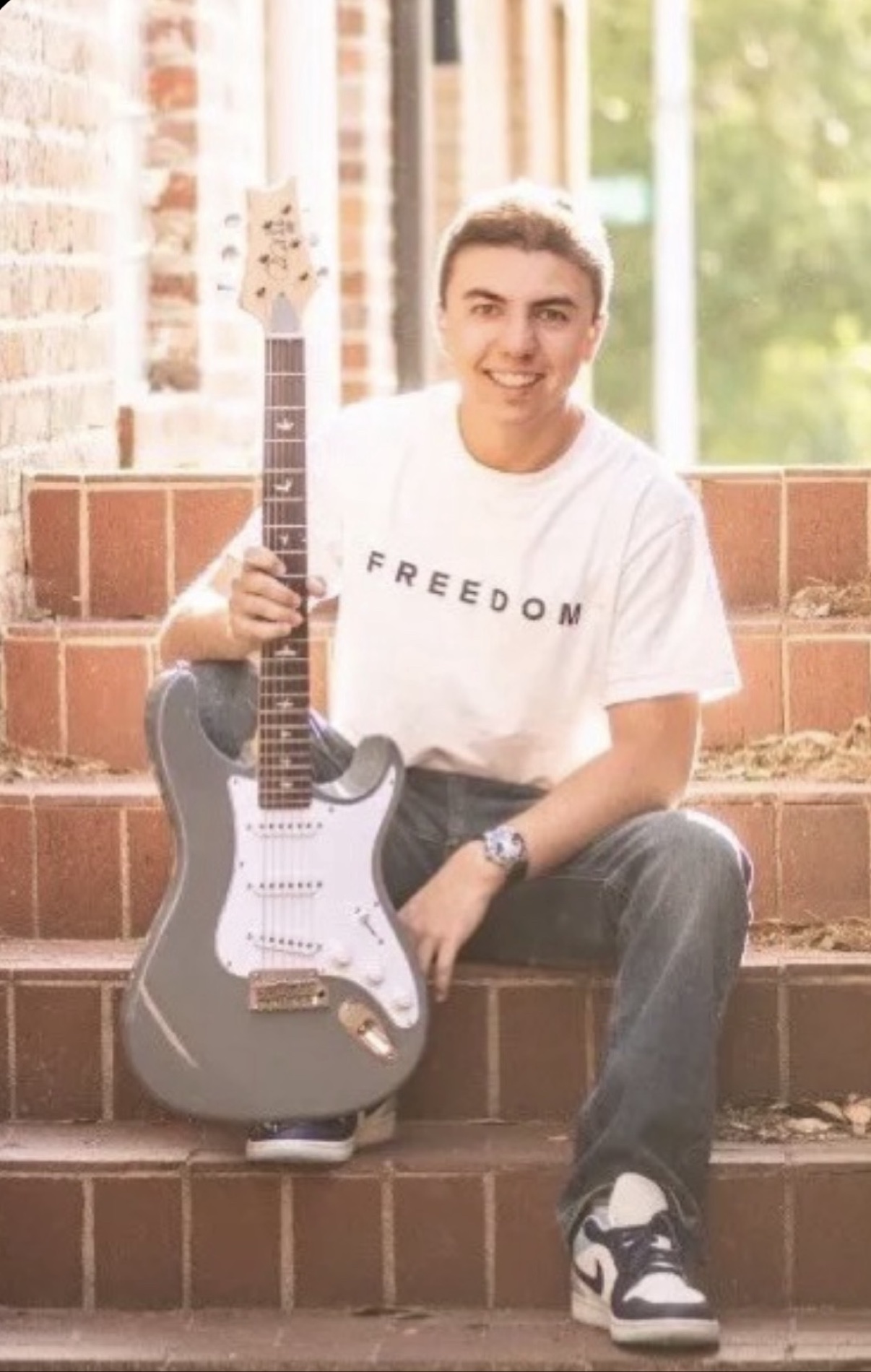 Wyatt sitting on brick steps holding his electric guitar