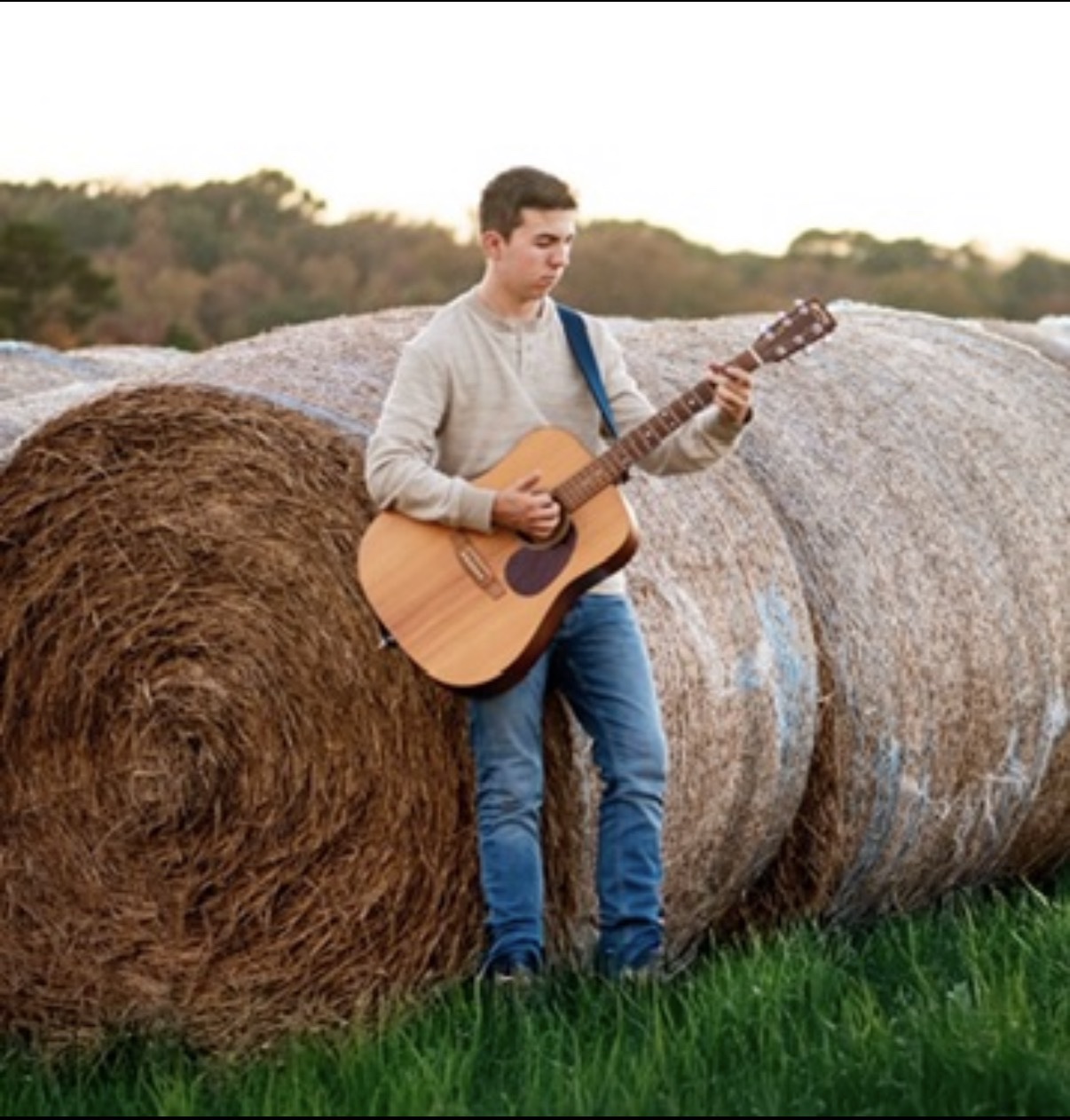 Wyatt playing his acoustic guitar outdoors by hay bales