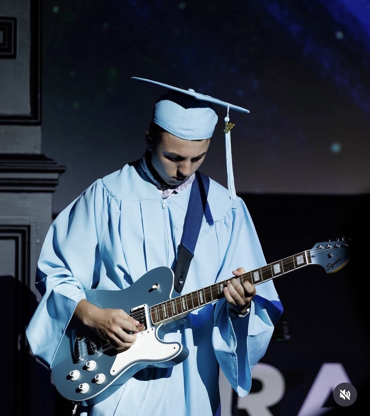 Wyatt playing electric guitar on stage in his graduation gown